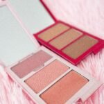Flat lay of elegant makeup palettes on pink fluffy surface with mirrors.